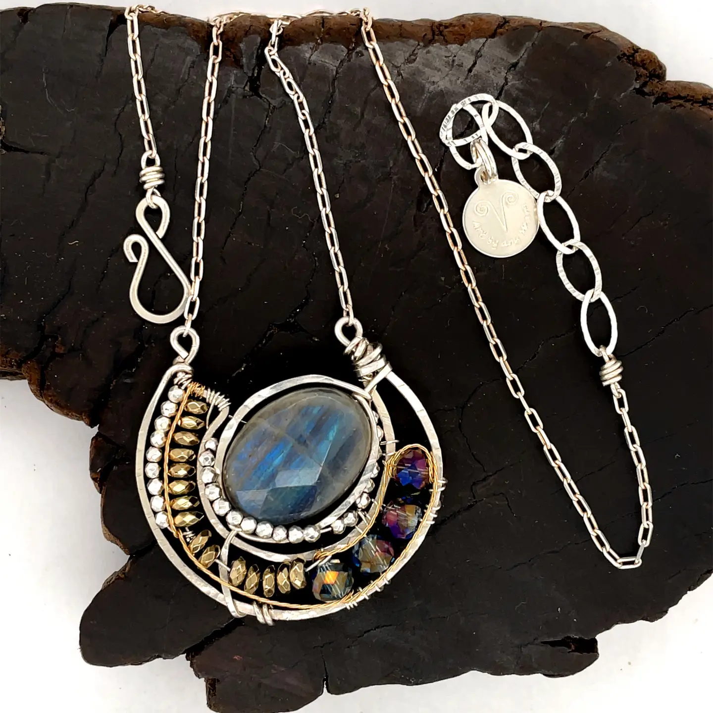 Faceted labradorite oval gemstones within a sterling silver pendant filled with pyrite gemstones and blue purple crystals and brass twist wire