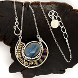 Faceted labradorite oval gemstones within a sterling silver pendant filled with pyrite gemstones and blue purple crystals and brass twist wire