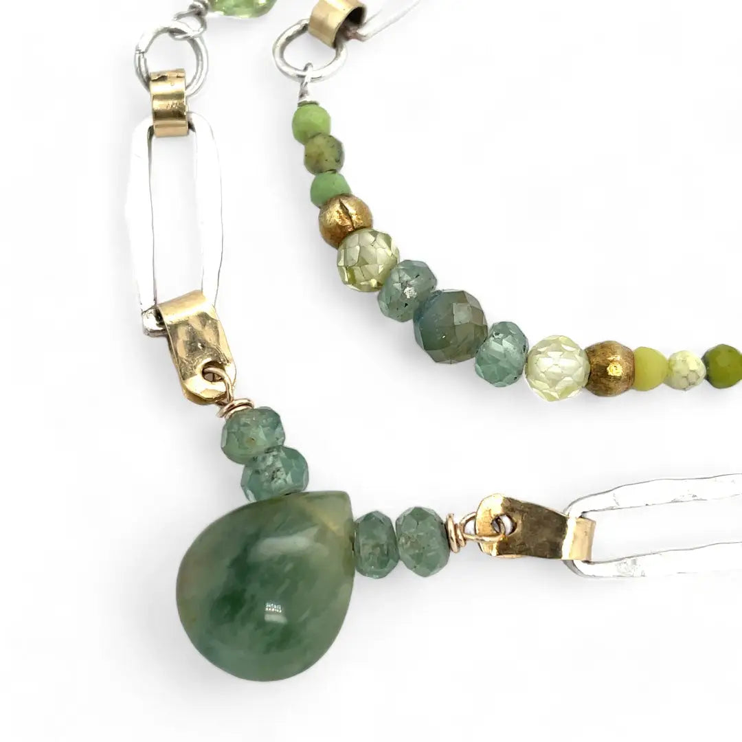 A double chain necklace with handmade hammered sterling silver rectangles and brass rings and straps, with green amethyst, green kyanite, crystal, cubic zirconia, and african metal beads