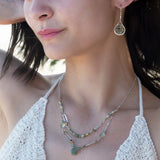 A double chain necklace with handmade hammered sterling silver rectangles and brass rings and straps, with green amethyst, green kyanite, crystal, cubic zirconia, and african metal beads