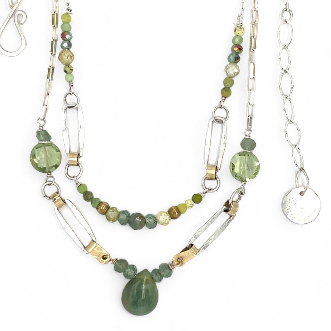 A double chain necklace with handmade hammered sterling silver rectangles and brass rings and straps, with green amethyst, green kyanite, crystal, cubic zirconia, and african metal beads