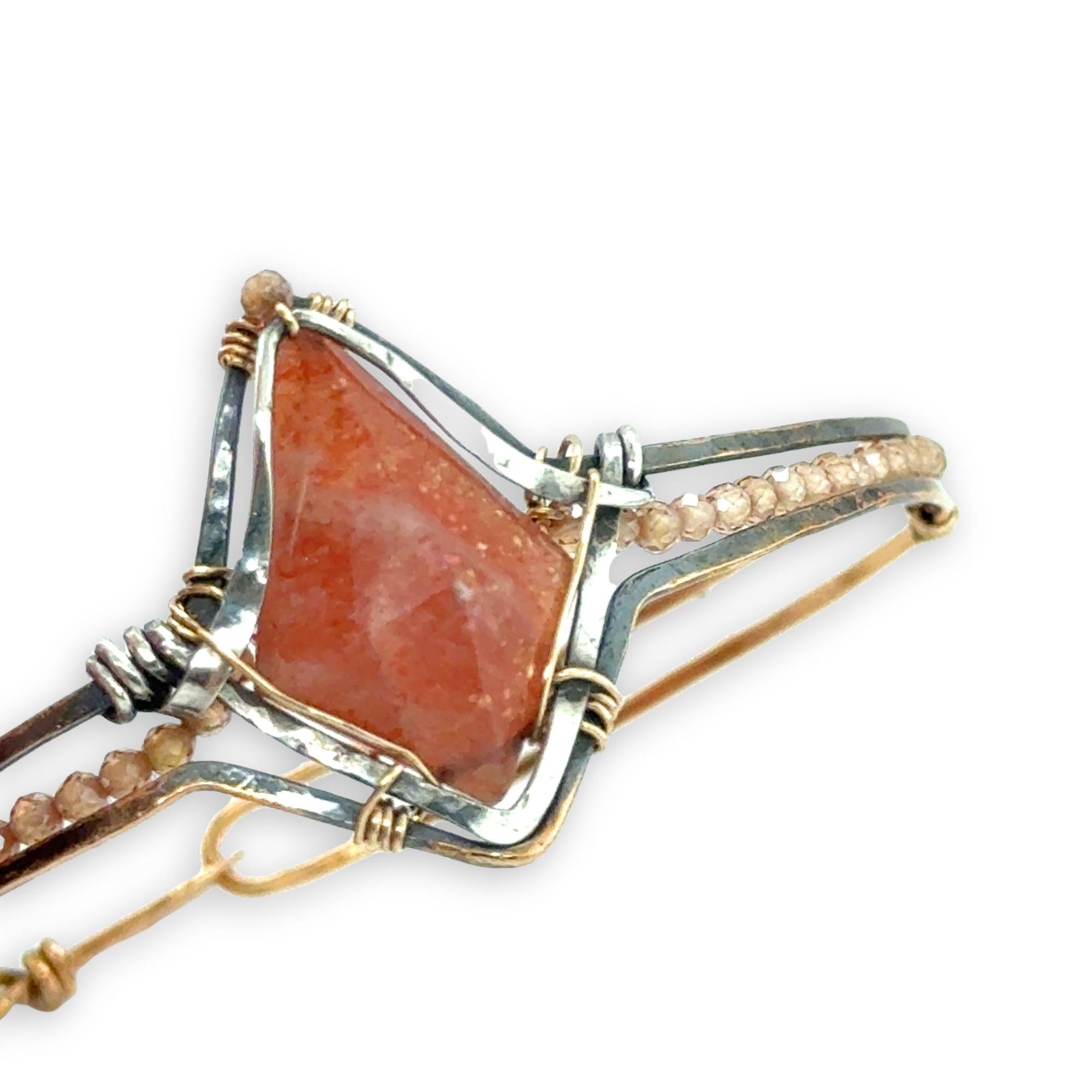 Bronze cuff bracelet with a darkened center carrying a stud cut sunstone diamond surrounded by sterling silver hammered wire and gold filled wire, accented by peach sparkly cubic zirconia