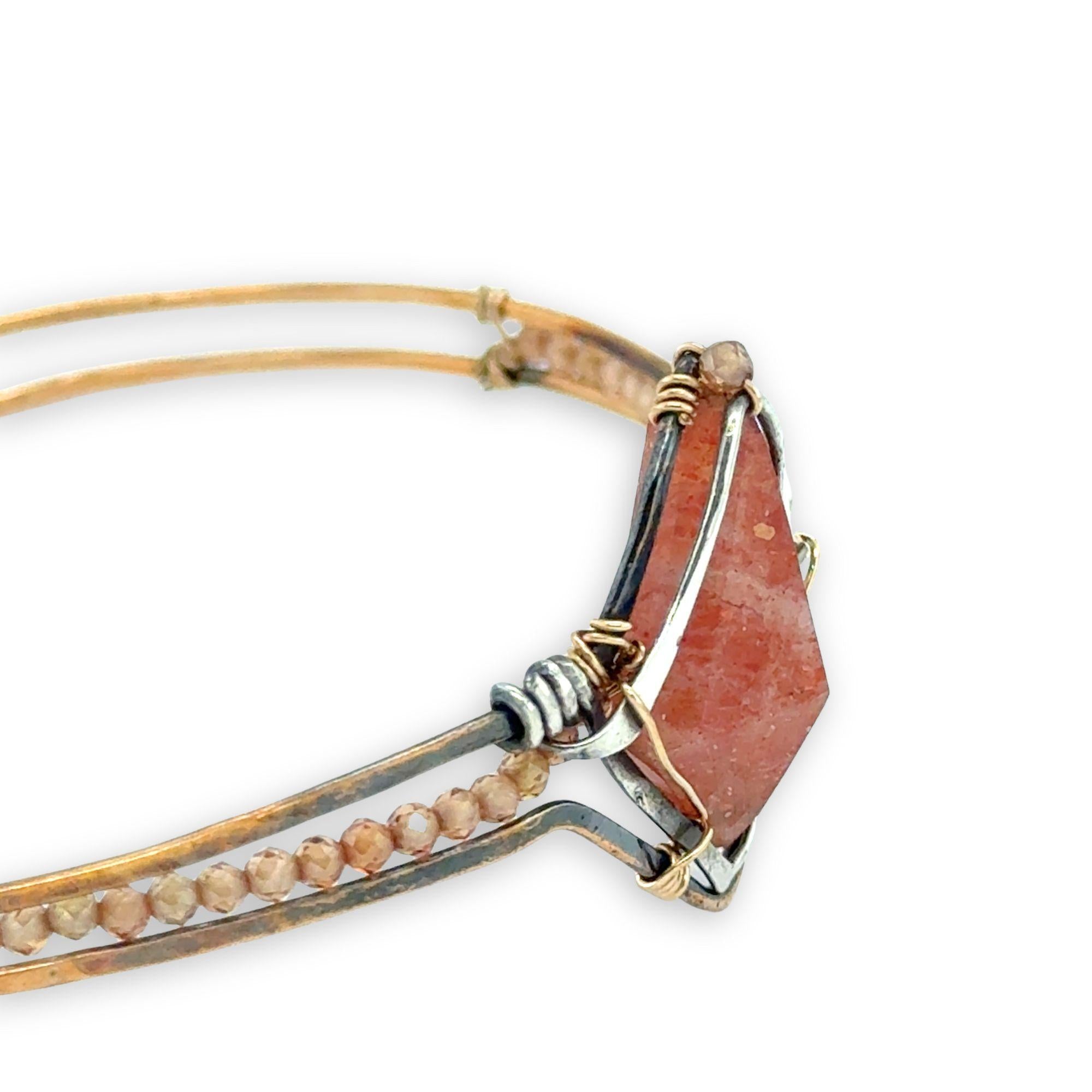 Bronze cuff bracelet with a darkened center carrying a stud cut sunstone diamond surrounded by sterling silver hammered wire and gold filled wire, accented by peach sparkly cubic zirconia