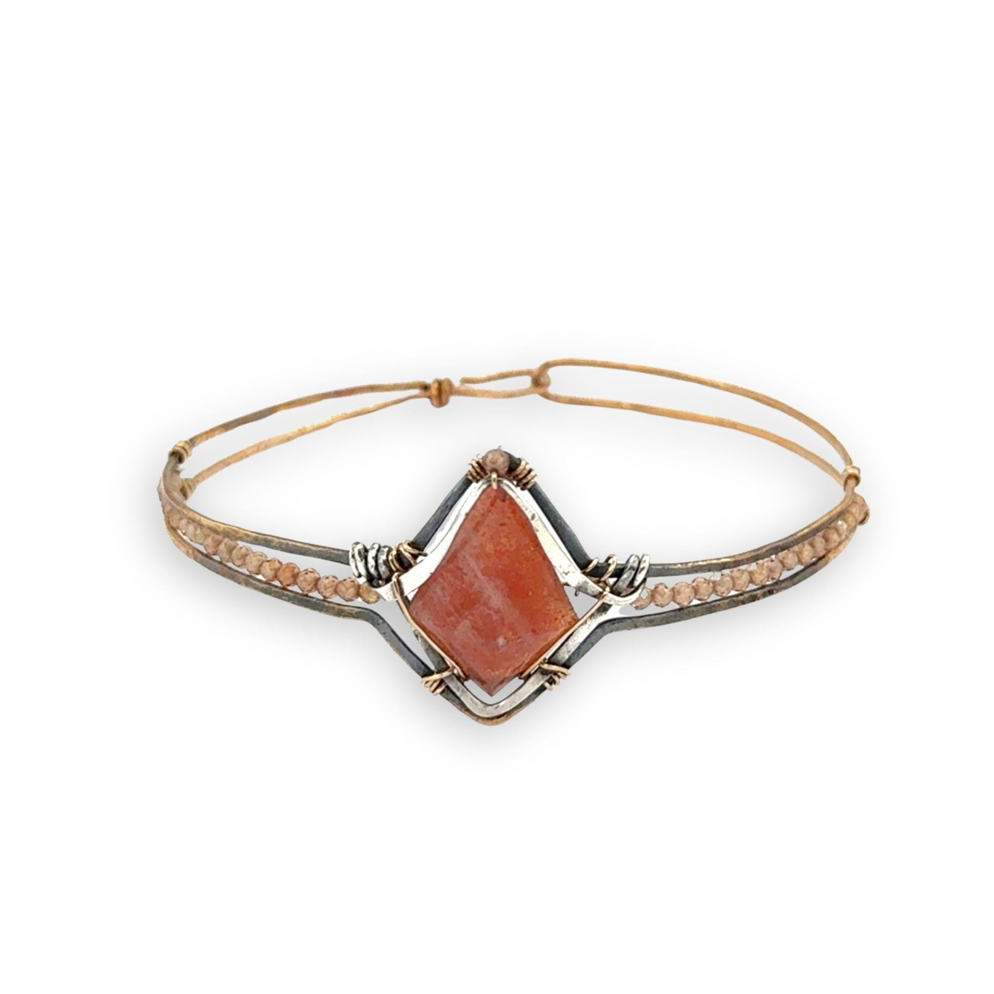 Bronze cuff bracelet with a darkened center carrying a stud cut sunstone diamond surrounded by sterling silver hammered wire and gold filled wire, accented by peach sparkly cubic zirconia