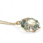 A brass hammered hexagon pendant necklace with a central pearl surrounded by a spiral of rutilated quartz and green kyanite gemstones, on a gold-filled rolo chain 
