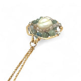 A brass hammered hexagon pendant necklace with a central pearl surrounded by a spiral of rutilated quartz and green kyanite gemstones, on a gold-filled rolo chain 