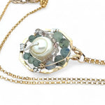 A brass hammered hexagon pendant necklace with a central pearl surrounded by a spiral of rutilated quartz and green kyanite gemstones, on a gold-filled rolo chain 