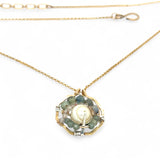 A brass hammered hexagon pendant necklace with a central pearl surrounded by a spiral of rutilated quartz and green kyanite gemstones, on a gold-filled rolo chain 