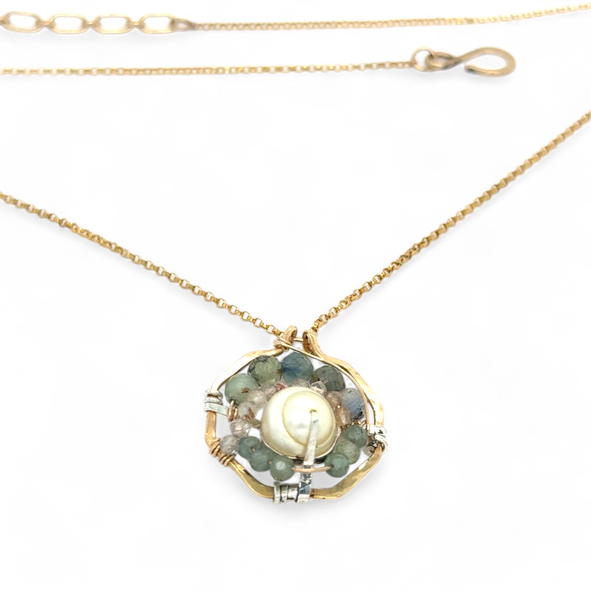A brass hammered hexagon pendant necklace with a central pearl surrounded by a spiral of rutilated quartz and green kyanite gemstones, on a gold-filled rolo chain 
