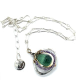 A necklace featuring a hand made thistle-shaped pendant with a green amethyst faceted drop gemstone and micro faceted lavender cubic zirconia gemstones, on a sterling silver bar chain.