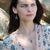 A necklace featuring a hand made thistle-shaped pendant with a green amethyst faceted drop gemstone and micro faceted lavender cubic zirconia gemstones, on a sterling silver bar chain.