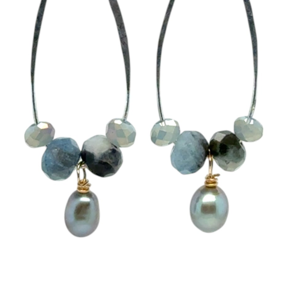 A pair of handmade sterling silver drop earrings with aquamarine faceted gemstones, crystals, and silvery freshwater pearls dangle from gold-filled accents.