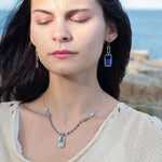 A pair of sterling silver box earrings with ocean blue crystal tiles wrapped in gold filled wire, hanging from a textured sterling silver link