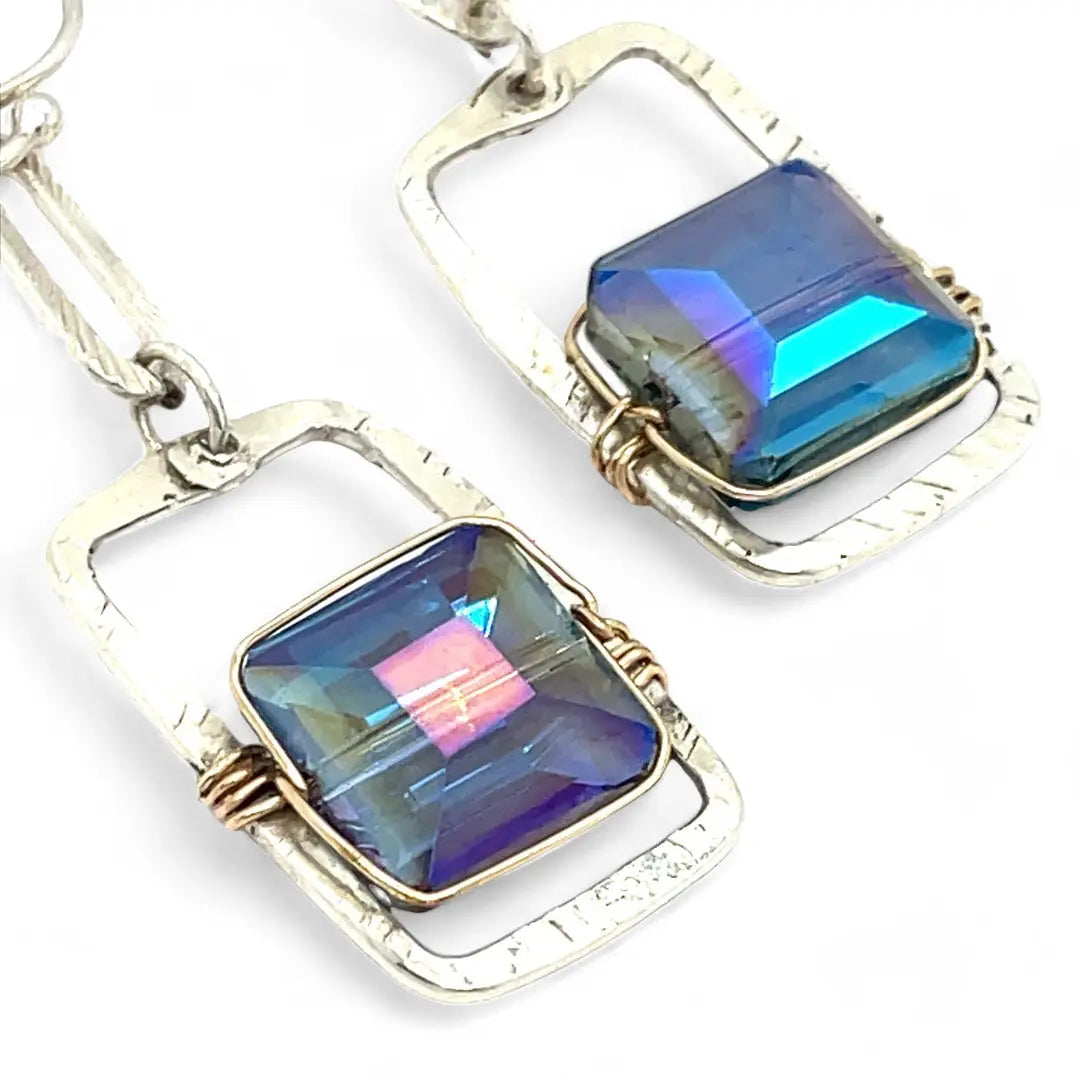 A pair of sterling silver box earrings with ocean blue crystal tiles wrapped in gold filled wire, hanging from a textured sterling silver link