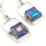 A pair of sterling silver box earrings with ocean blue crystal tiles wrapped in gold filled wire, hanging from a textured sterling silver link