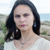 A pair of sterling silver box earrings with ocean blue crystal tiles wrapped in gold filled wire, hanging from a textured sterling silver link