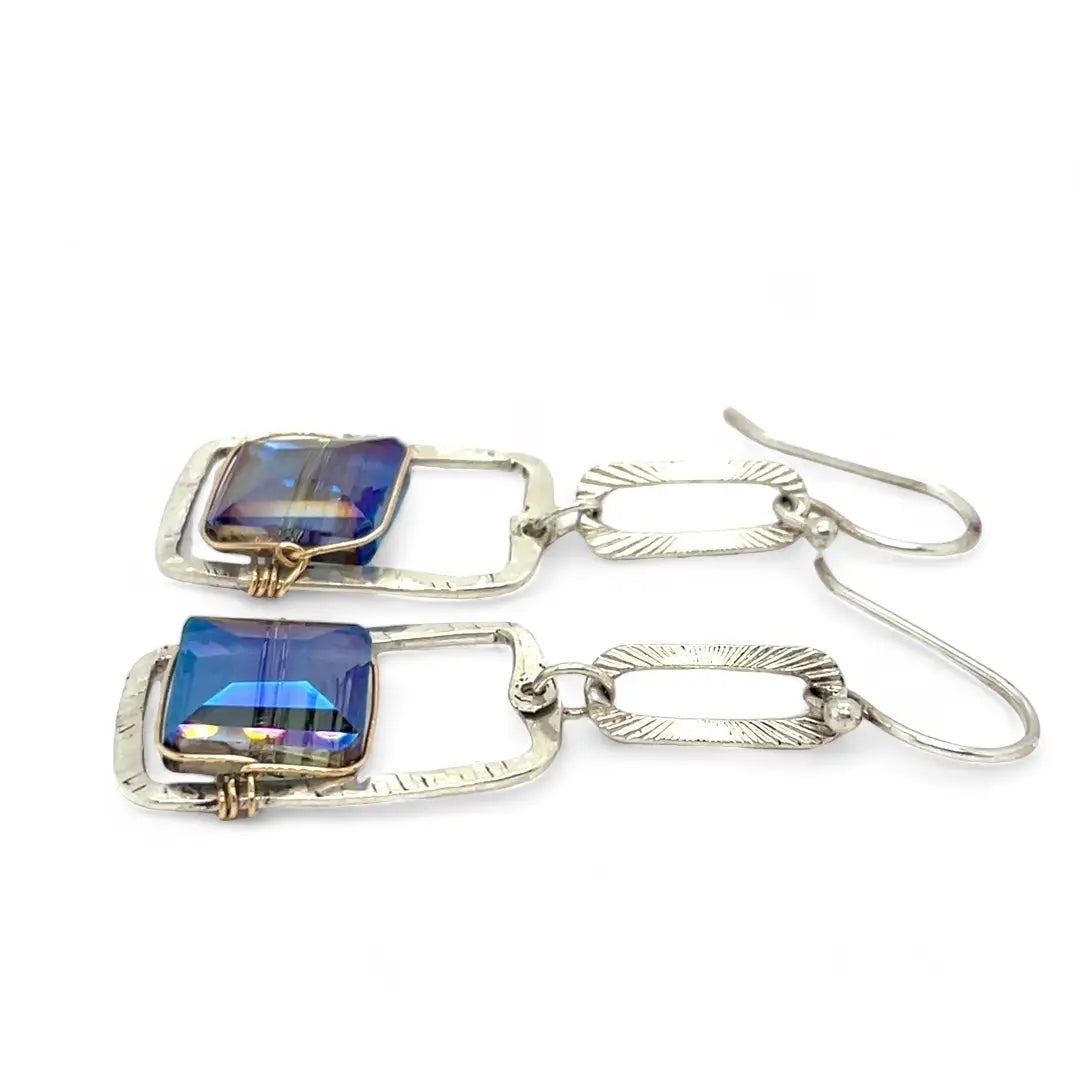 A pair of sterling silver box earrings with ocean blue crystal tiles wrapped in gold filled wire, hanging from a textured sterling silver link