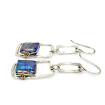 A pair of sterling silver box earrings with ocean blue crystal tiles wrapped in gold filled wire, hanging from a textured sterling silver link