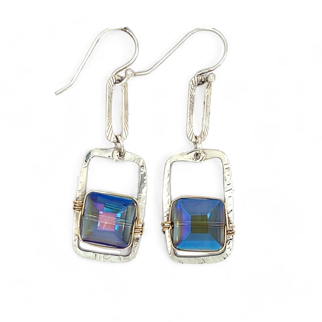 A pair of sterling silver box earrings with ocean blue crystal tiles wrapped in gold filled wire, hanging from a textured sterling silver link