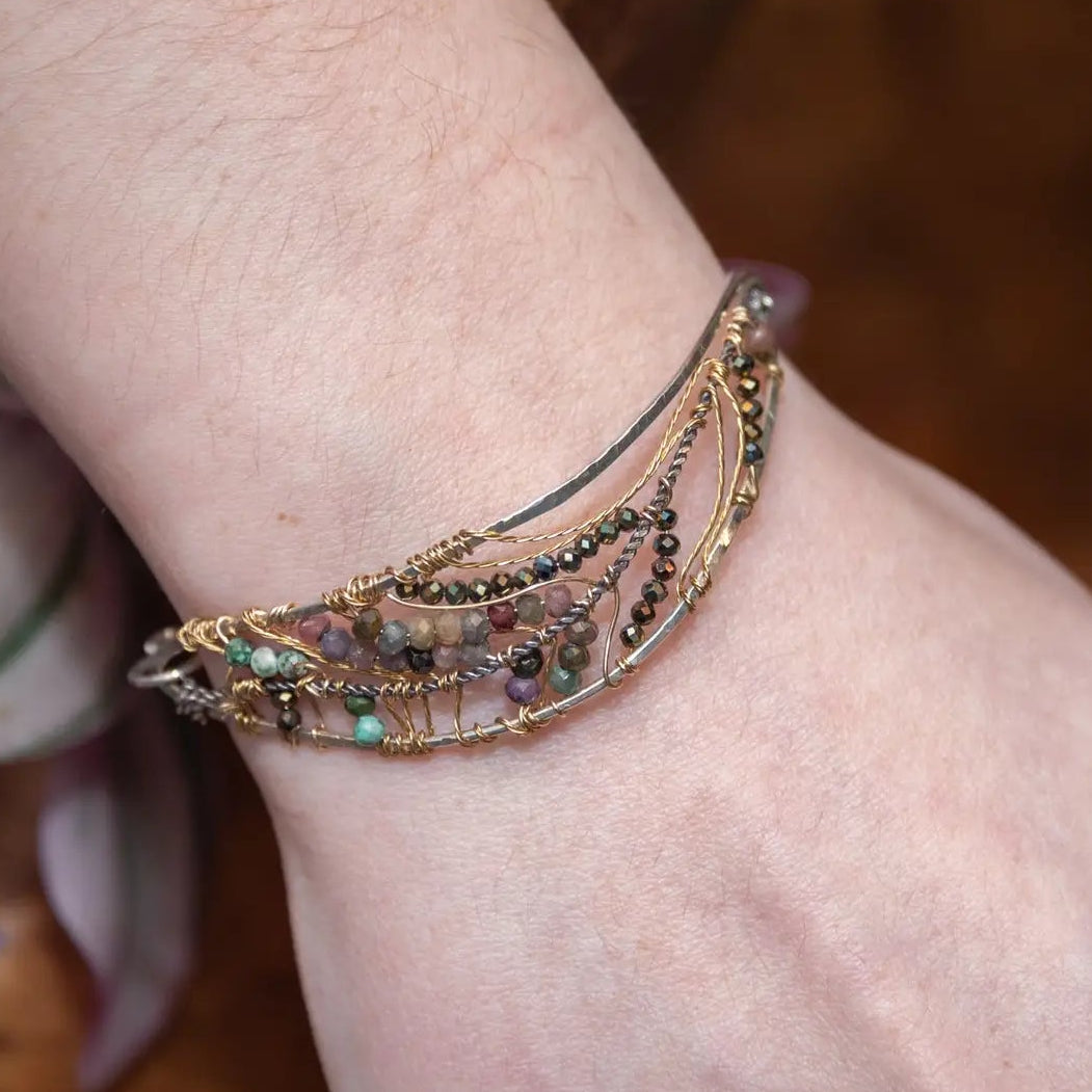 A sterling silver wave shaped bracelet embellished with faceted tourmaline and pyrite gemstones on gold filled wire and brass twist accents