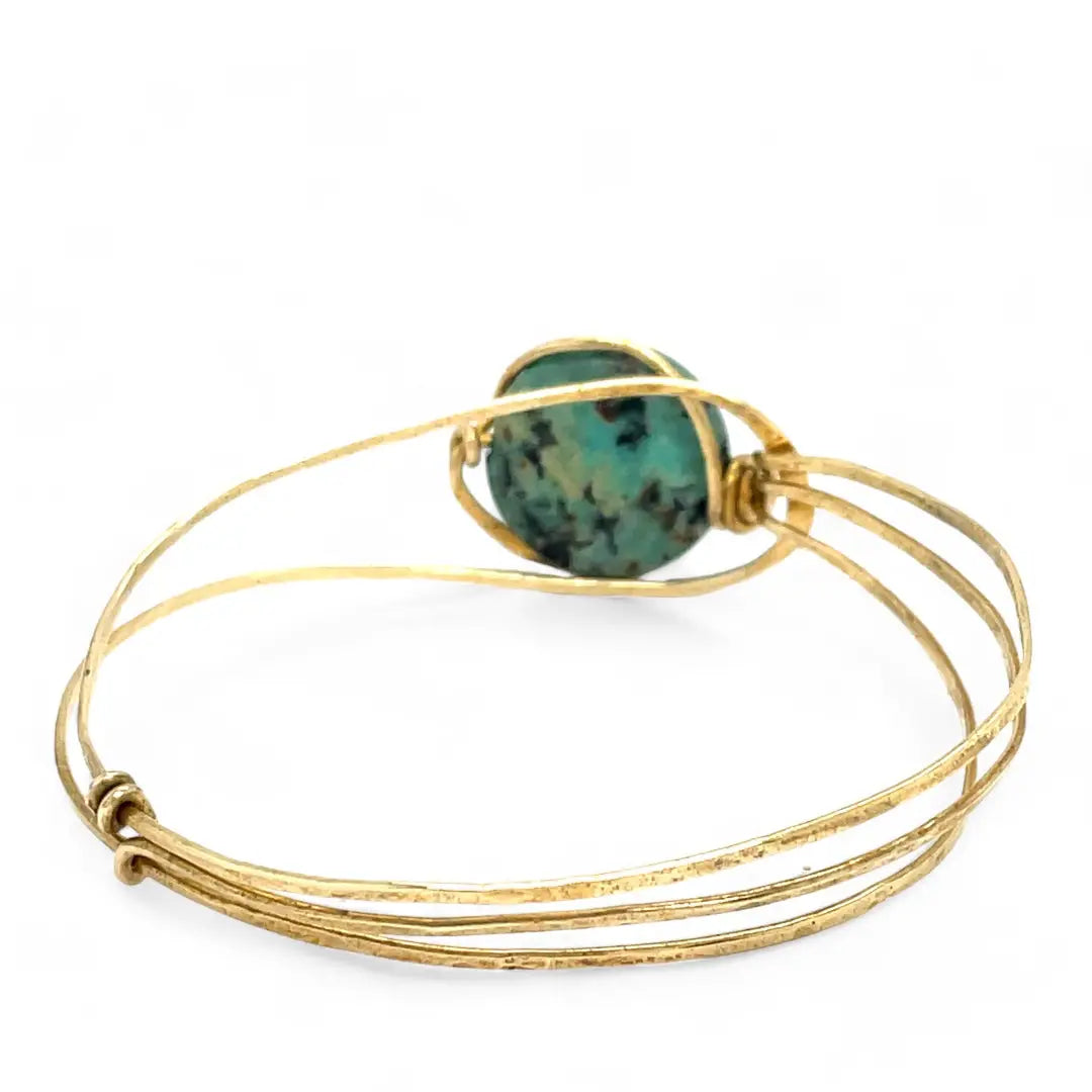 a turquoise smooth coin gemstone set in a hammered brass cuff bracelet, featuring a hand-formed clasp.