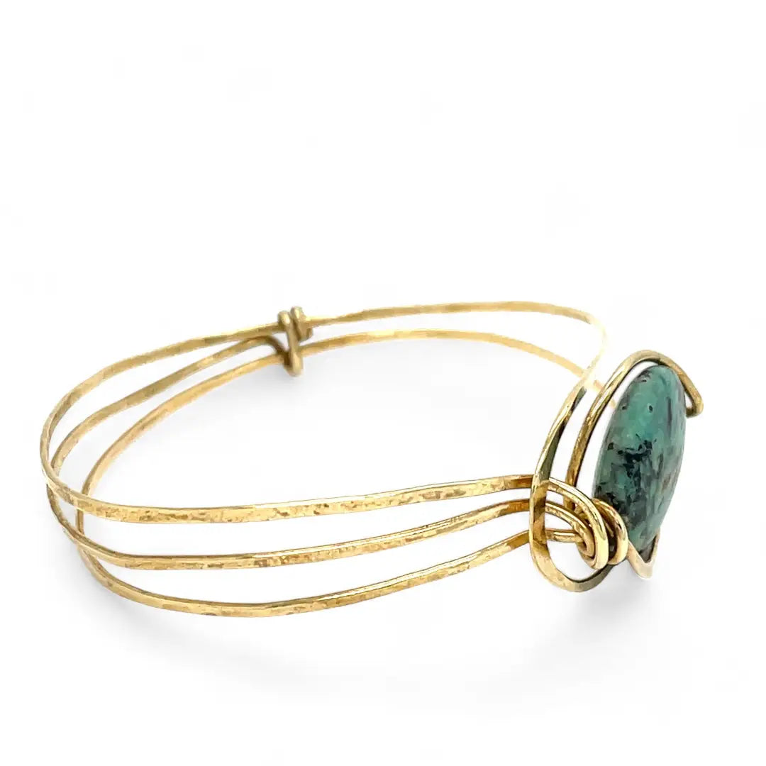 a turquoise smooth coin gemstone set in a hammered brass cuff bracelet, featuring a hand-formed clasp.