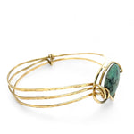 a turquoise smooth coin gemstone set in a hammered brass cuff bracelet, featuring a hand-formed clasp.