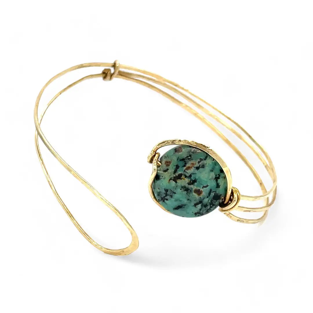 a turquoise smooth coin gemstone set in a hammered brass cuff bracelet, featuring a hand-formed clasp.