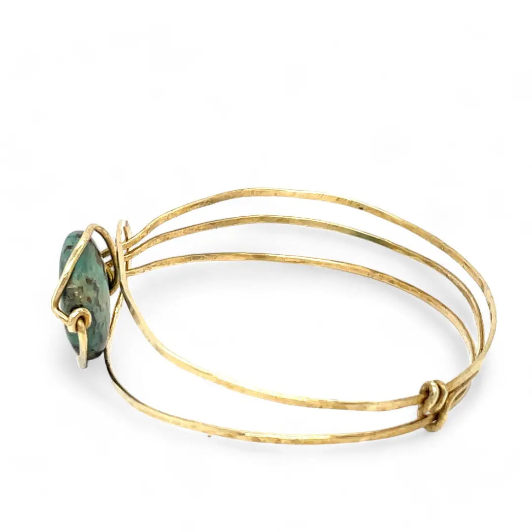 a turquoise smooth coin gemstone set in a hammered brass cuff bracelet, featuring a hand-formed clasp.