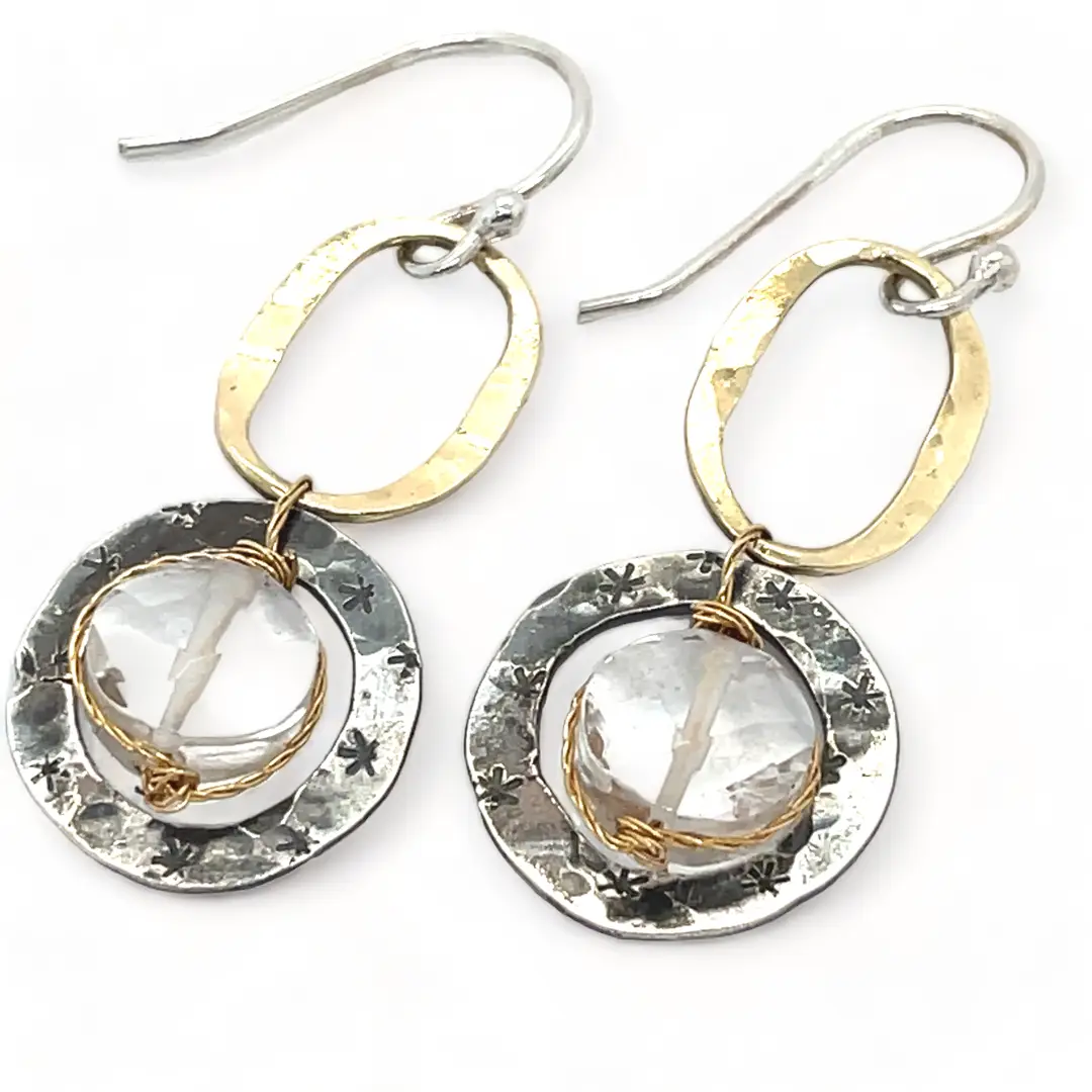 A pair of earrings featuring clear faceted quartz gemstones, oxidized sterling silver stamped rings on brass hammered handmade links.