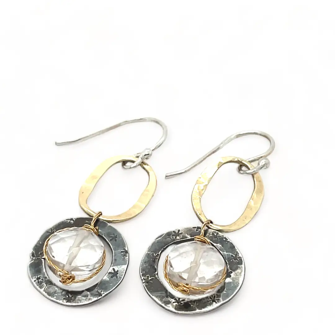 A pair of earrings featuring clear faceted quartz gemstones, oxidized sterling silver stamped rings on brass hammered handmade links.