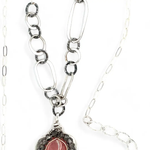 A sterling silver mini cameo pendant necklace with a salmon rhodochrosite center, wrapped in gold filled, surrounded by tourmalinated quartz gemstones. The necklace has an oxidized textured chain with hand made chain links.