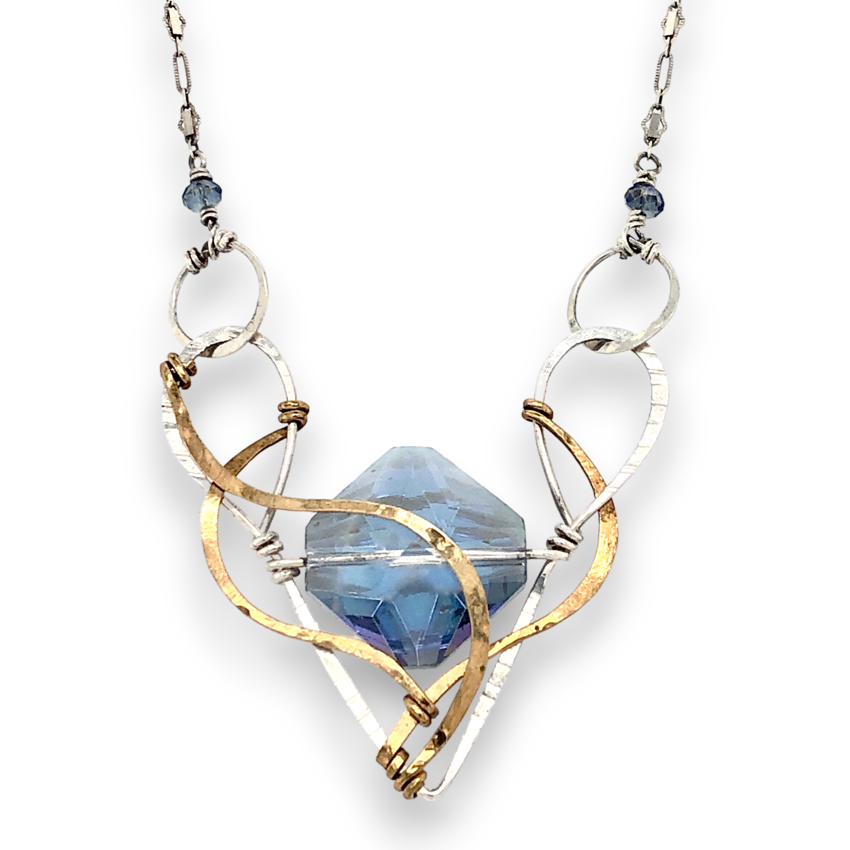 A blue diamond cut crystal is centered within a sterling silver v pendant with brass swirls on a sterling silver chain with blue crystal accents