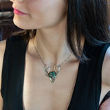 A turquoise coin gemstone sits in a hammered brass and sterling silver oxidized necklace on sterling silver bar chain