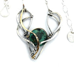 A turquoise coin gemstone sits in a hammered brass and sterling silver oxidized necklace on sterling silver bar chain