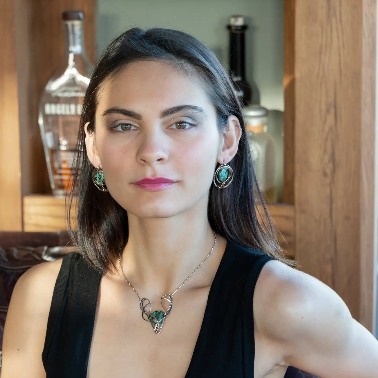 A turquoise coin gemstone sits in a hammered brass and sterling silver oxidized necklace on sterling silver bar chain