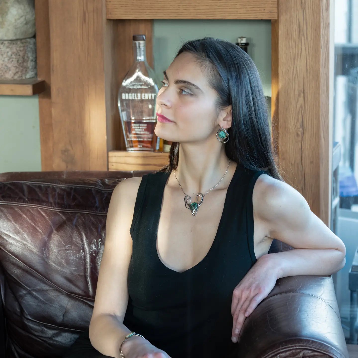 A turquoise coin gemstone sits in a hammered brass and sterling silver oxidized necklace on sterling silver bar chain