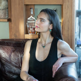 A turquoise coin gemstone sits in a hammered brass and sterling silver oxidized necklace on sterling silver bar chain