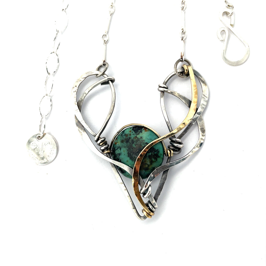 A turquoise coin gemstone sits in a hammered brass and sterling silver oxidized necklace on sterling silver bar chain