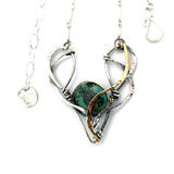 A turquoise coin gemstone sits in a hammered brass and sterling silver oxidized necklace on sterling silver bar chain