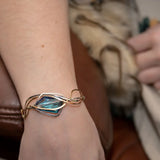 A large blue crystal is nestled within layers of braided hammered sterling silver, brass, and bronze wires to form a handmade statement cuff bracelet