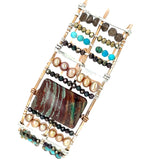 A wide bronze cuff bracelet featuring a combination of striped jasper, fresh water pearls, pyrite, smokey quartz, and turquoise gemstones, strung on sterling silver and hammered bronze.