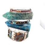 A wide bronze cuff bracelet featuring a combination of striped jasper, fresh water pearls, pyrite, smokey quartz, and turquoise gemstones, strung on sterling silver and hammered bronze.