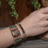 A wide bronze cuff bracelet featuring a combination of striped jasper, fresh water pearls, pyrite, smokey quartz, and turquoise gemstones, strung on sterling silver and hammered bronze.