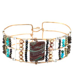 A wide bronze cuff bracelet featuring a combination of striped jasper, fresh water pearls, pyrite, smokey quartz, and turquoise gemstones, strung on sterling silver and hammered bronze.