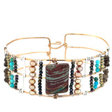 A wide bronze cuff bracelet featuring a combination of striped jasper, fresh water pearls, pyrite, smokey quartz, and turquoise gemstones, strung on sterling silver and hammered bronze.