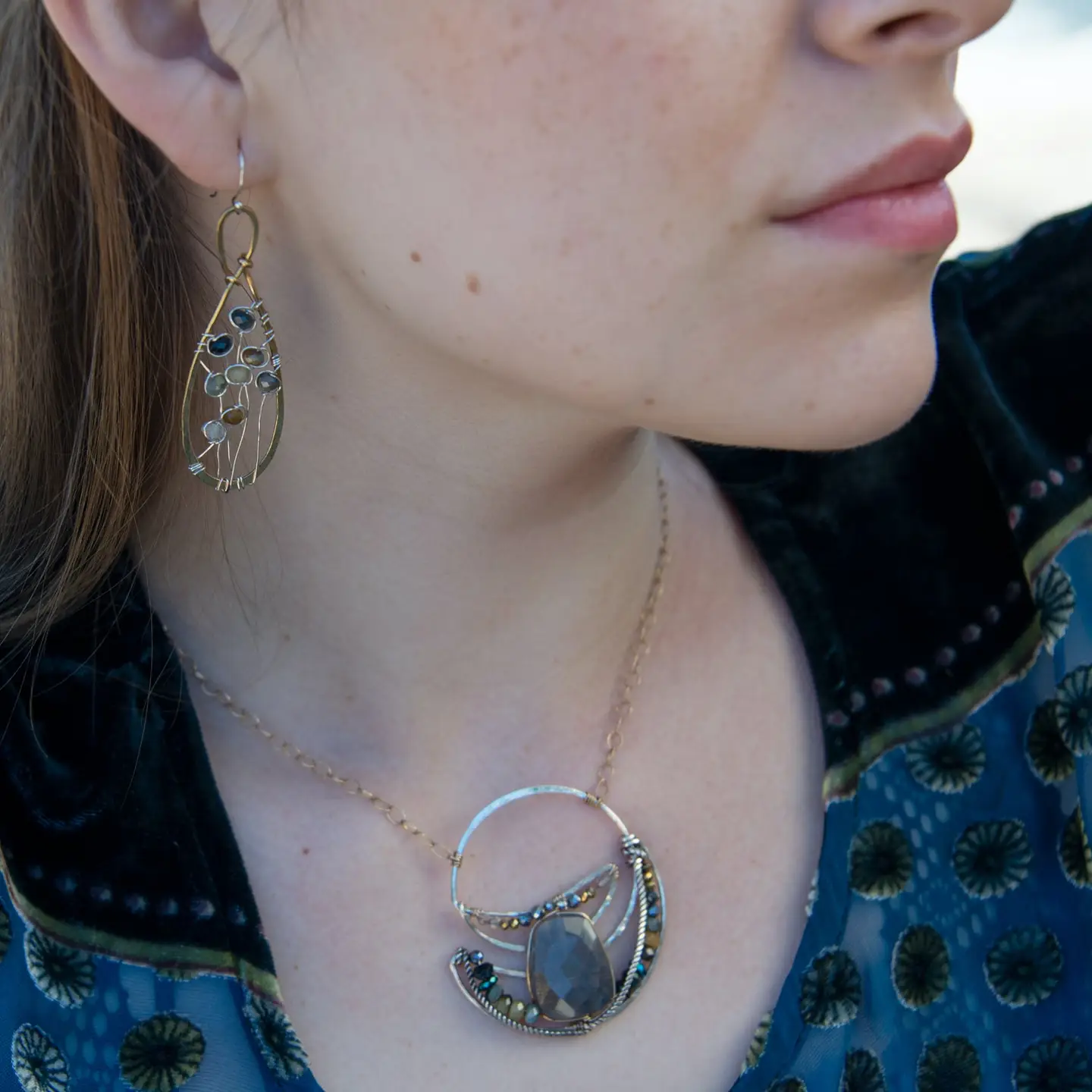 A pair of brass infinity shaped earrings featuring multicolored cat's eye faceted gemstones  and sterling silver details. Natural shades of yellow, blue, and green