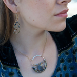 A pair of brass infinity shaped earrings featuring multicolored cat's eye faceted gemstones  and sterling silver details. Natural shades of yellow, blue, and green