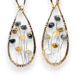 A pair of brass infinity shaped earrings featuring multicolored cat's eye faceted gemstones  and sterling silver details. Natural shades of yellow, blue, and green