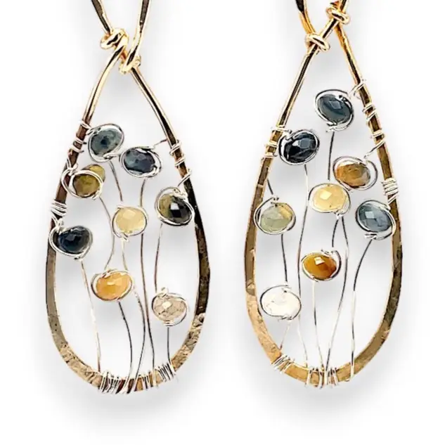 A pair of brass infinity shaped earrings featuring multicolored cat's eye faceted gemstones  and sterling silver details. Natural shades of yellow, blue, and green
